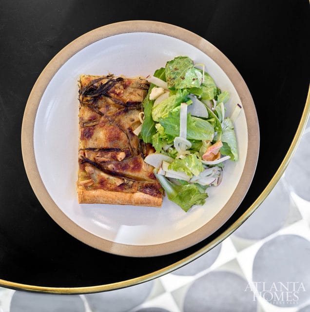 Slice of quiche with caramelized onions and a side salad on a white plate with a tan rim.
