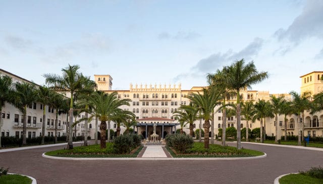 Large white building with ornate details, palm trees, and a fountain entrance
