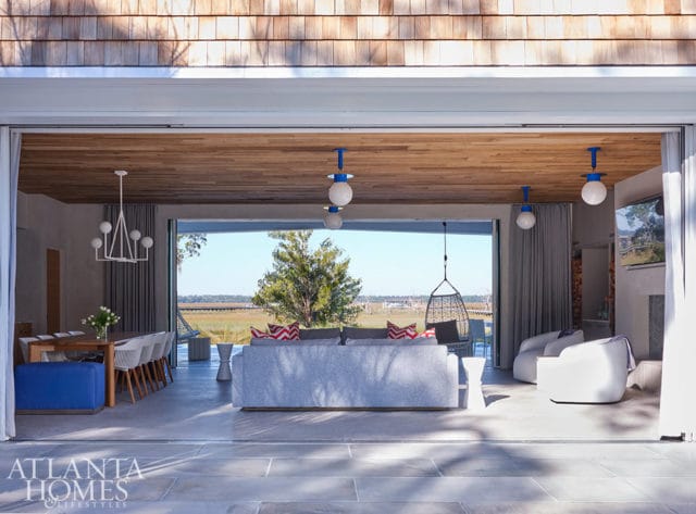 Living room with gray sofa, white chairs, and wood ceiling, opening to a marsh view.