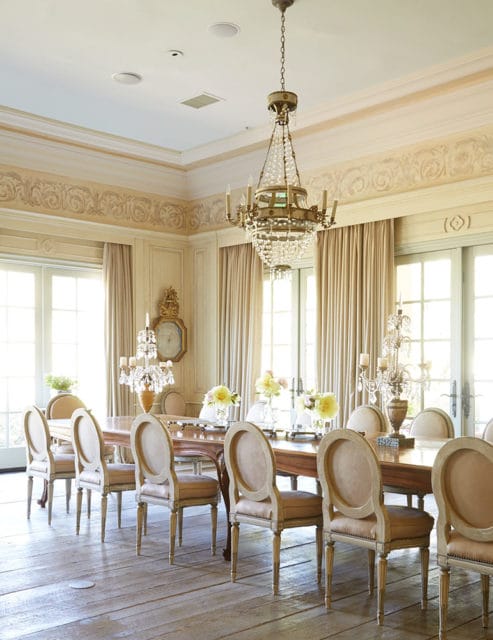 Dining room with a long wooden table, upholstered chairs, and a crystal chandelier.