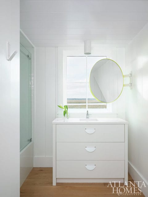 White bathroom vanity with three drawers and a round mirror with a lime green frame.
