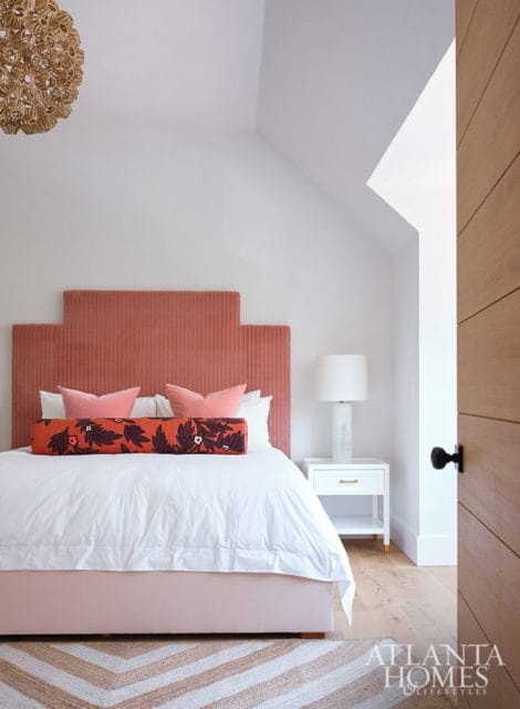Bedroom with coral headboard, white bedding, and patterned bolster pillow.