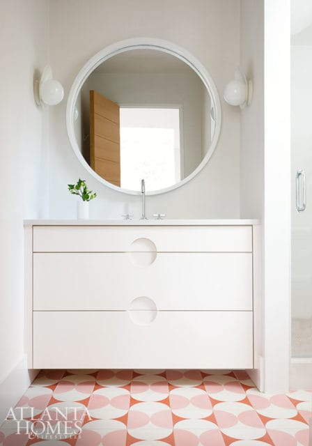 White vanity with circular pulls, white countertop, and round mirror. Pink and white geometric