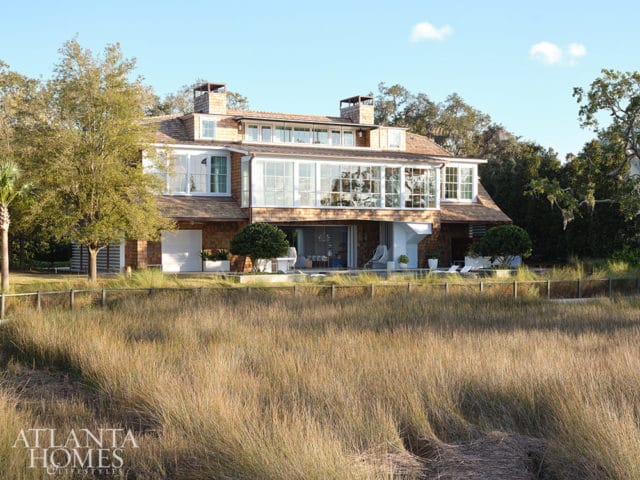Coastal home with cedar shingles, large windows, and a marsh in the foreground.