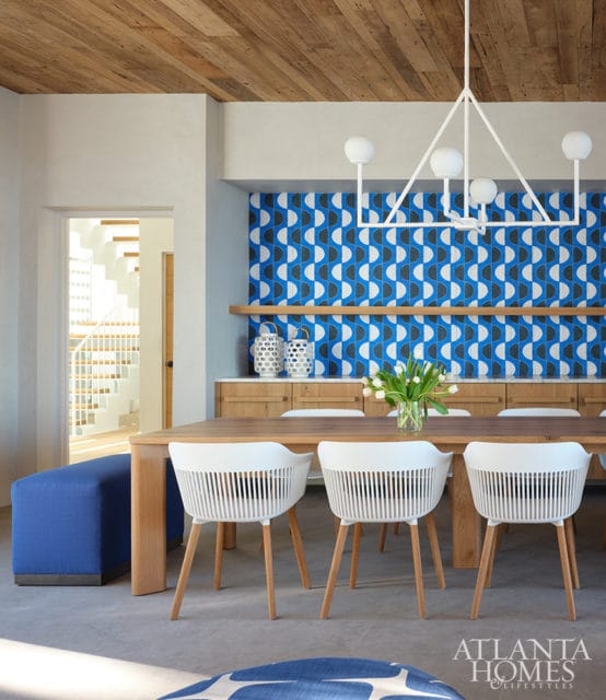 Dining room with blue geometric wallpaper, wood table, and white chairs.