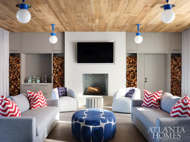 Living room with gray sofas, white chairs, blue ottoman, and stacked firewood.
