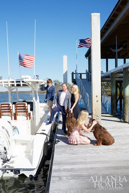 Family with two dogs on a dock next to a boat, with American flags flying.