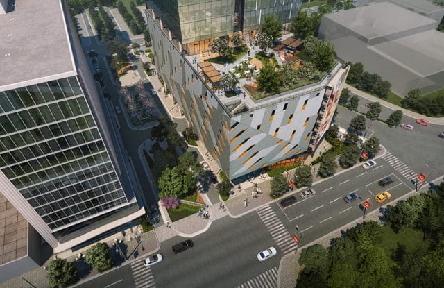 Modern building with geometric facade and rooftop garden, surrounded by trees and city streets.