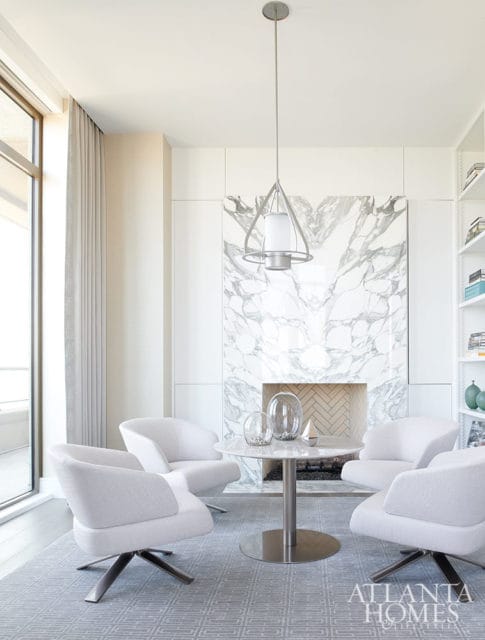 Living room with white chairs around a marble table in front of a marble fireplace.