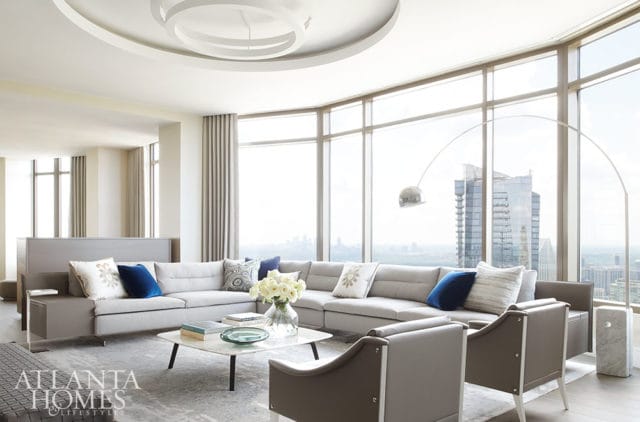 Gray sectional sofa with blue and patterned pillows, marble coffee table, and arc floor lamp