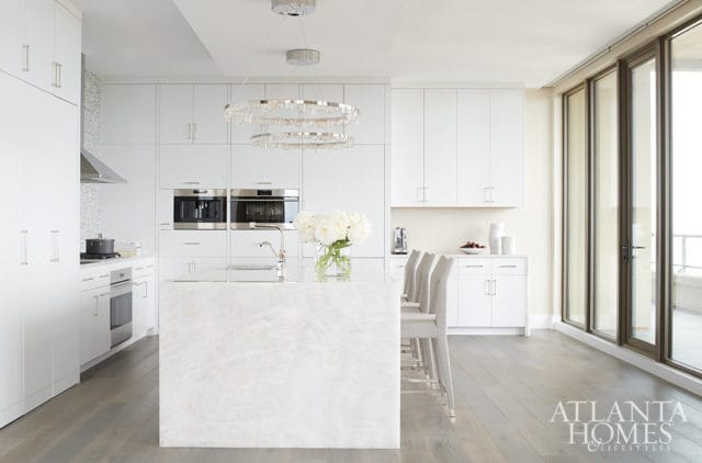 White kitchen with marble island, stainless steel appliances, and modern chandelier.