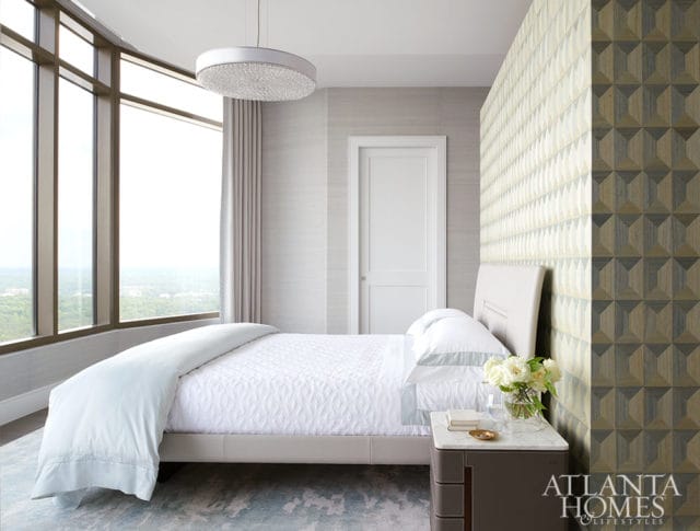 Bedroom with white bedding, geometric wallpaper, and large windows overlooking a cityscape.