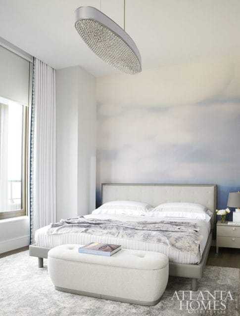 Bedroom with upholstered bed, patterned throw, tufted bench, and cloud mural