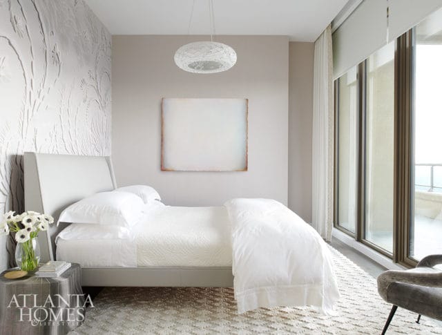Bedroom with white bedding, textured wallpaper, and large windows overlooking a balcony.