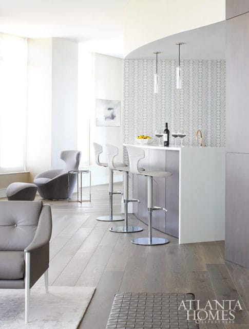 Modern kitchen bar with white stools, marble countertop, and patterned wallpaper.