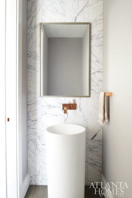 Powder room with white pedestal sink, marble tile walls, and brass faucet.