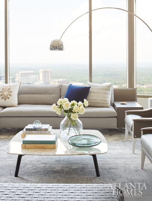 Gray sofa with decorative pillows and a modern arc lamp. White roses in a vase on a marble coffee