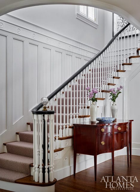 White paneled staircase with carpet runner, dark wood banister, and mahogany console table with
