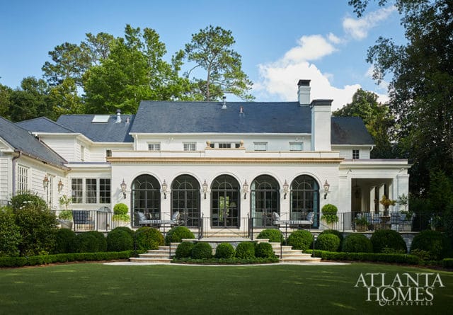White brick house with arched windows, dark roof, and manicured lawn. Atlanta Homes & Lifestyles