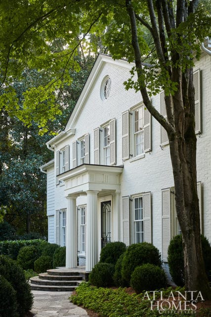 White brick house with shutters, columns, and a stone pathway.