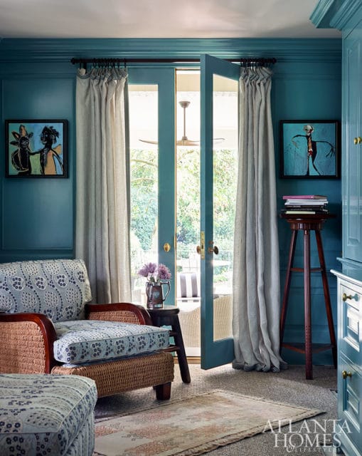 Teal paneled room with wicker armchair, patterned cushions, and double doors opening to a patio.