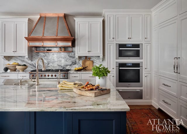 White kitchen with marble island, copper range hood, and double ovens.