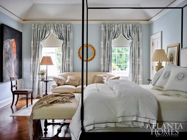 Bedroom with light blue walls, four-poster bed, patterned curtains, and sofa