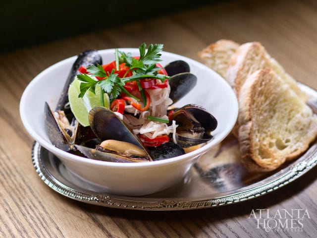 Bowl of mussels with lime, red peppers, and parsley, served with toast on a silver platter.