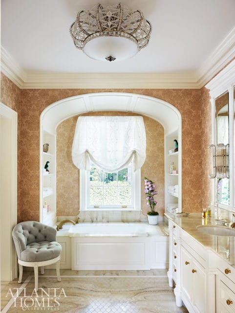 Elegant bathroom with a white soaking tub, ornate chandelier, and marble vanity.