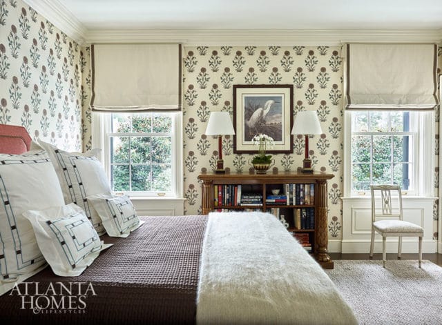 Bedroom with floral wallpaper, bed with white pillows, and a wooden bookshelf filled with books.