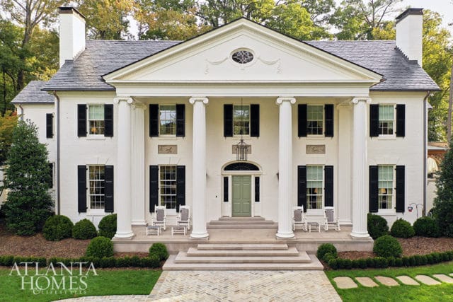 White neoclassical house with large columns, black shutters, and a green front door.