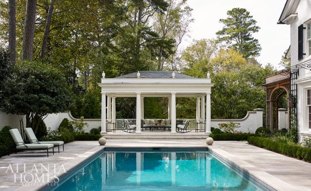 Poolside gazebo with seating, lounge chairs, and manicured hedges.