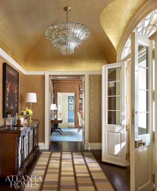 Hallway with gold leaf ceiling, glass chandelier, and patterned wallpaper.
