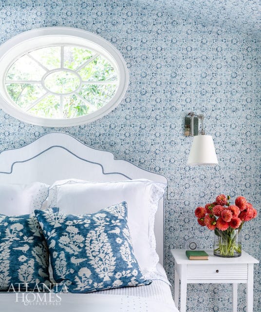 Bedroom with blue patterned wallpaper, white headboard, and blue floral pillows. Oval window.