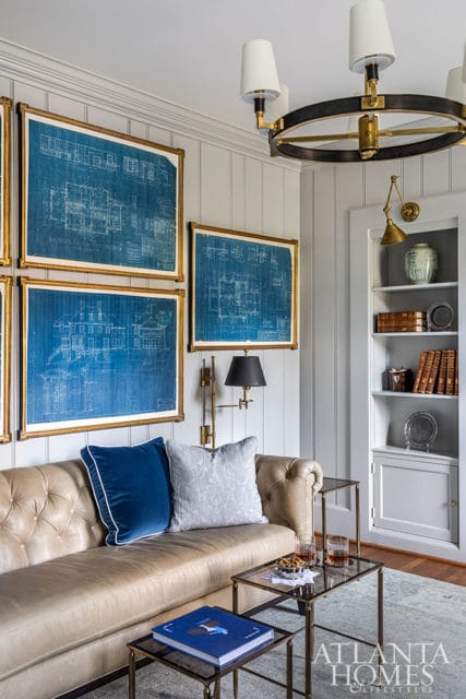 Living room with tufted leather sofa, blue and gray pillows, framed blueprints, and built-in