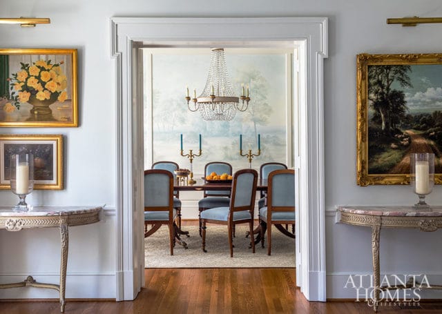 Dining room with blue upholstered chairs, crystal chandelier, and landscape mural