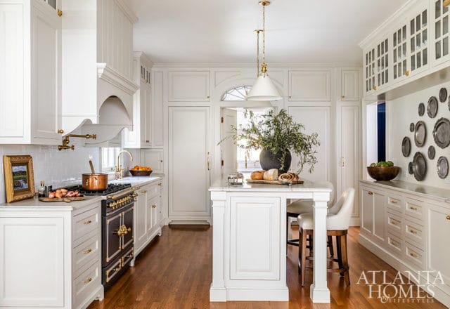 White kitchen with marble island, brass hardware, dark range, and pendant lights.