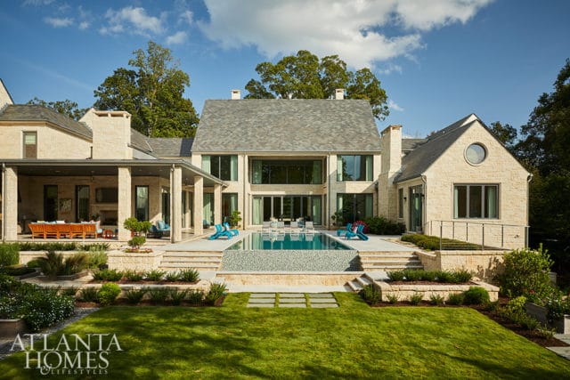 Stone mansion with pool, covered patio, and manicured lawn.