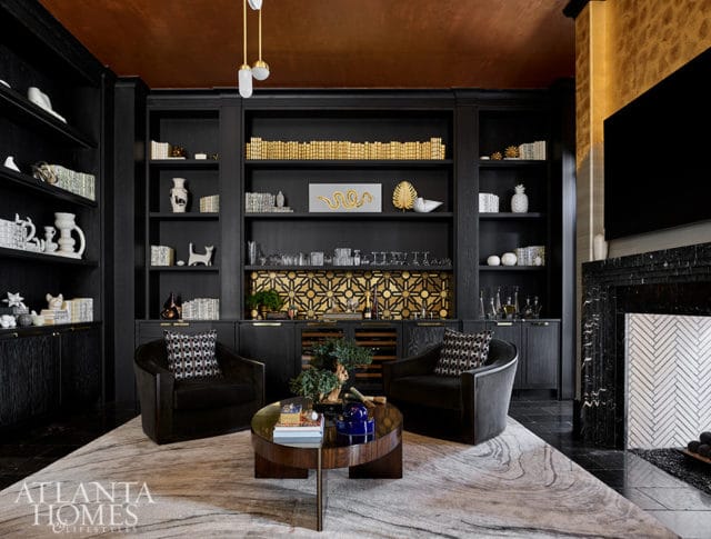 Dark wood built-in shelves with gold accents, two dark chairs, and a round coffee table.