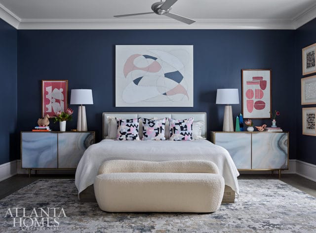 Bedroom with navy walls, white bedding, abstract art, and agate-patterned nightstands.