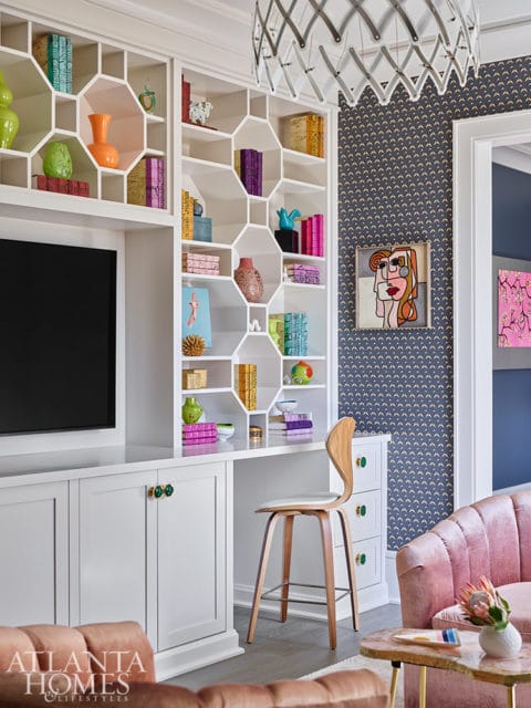 White built-in shelving unit with colorful books and decor, desk, and wooden stool.