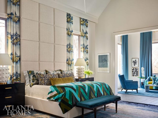 Bedroom with upholstered headboard, patterned curtains, and a teal, green, and brown geometric