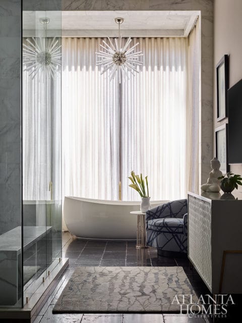 Bathroom with freestanding tub, patterned chair, and starburst chandelier.