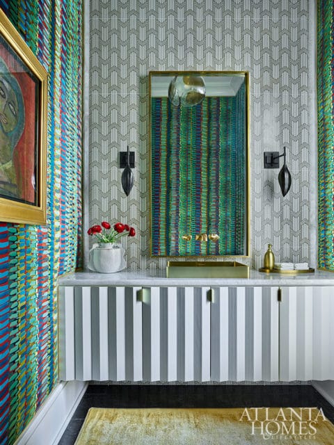 Bathroom with colorful patterned wallpaper, striped vanity, and gold mirror.