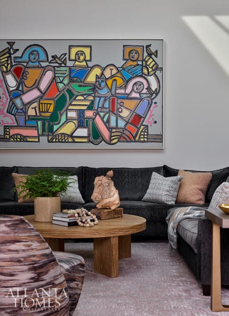Dark gray sectional sofa with colorful abstract art above. Round wood coffee table with sculpture