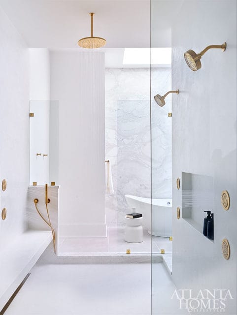 Modern white bathroom with brass showerheads, marble accents, and a freestanding tub.