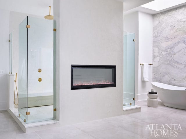 Modern bathroom with glass shower, freestanding tub, fireplace, and marble accent wall.