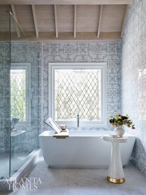Freestanding bathtub with a wooden tray holding a book and bowl, patterned tile walls, and a