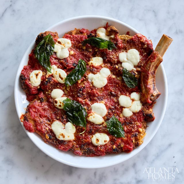 Breaded cutlet with marinara sauce, dollops of mozzarella, and basil leaves, served with a bone-in