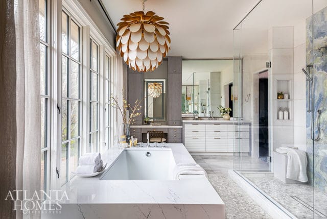 Modern bathroom with white soaking tub, marble accents, large windows, and glass shower with blue